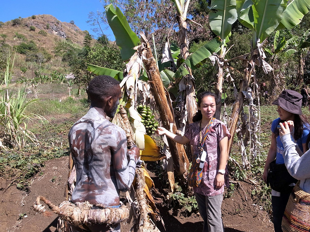 祭り装束の道案内さんとガイドさんがバナナの木を解説中、いろんな果物が植えられています